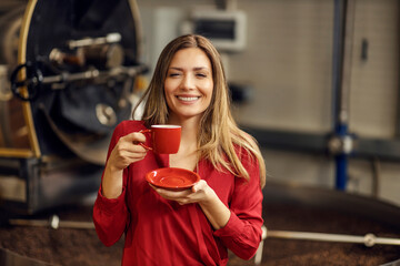 A happy woman holding cup of coffee in coffee factory.