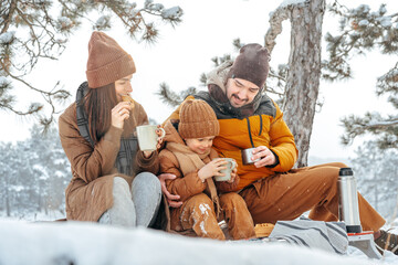 Happy family with cups of hot tea spending time together in winter forest