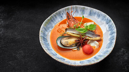Bouillabaisse soup with seafood on a plate, on a dark background