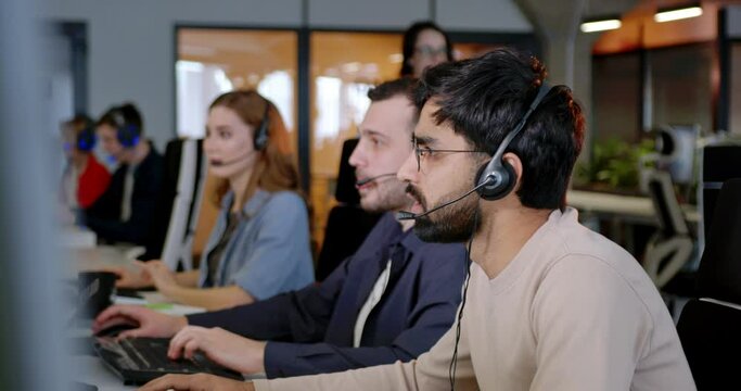 Handsome man working in call center and talking with client. Male worker in headset at support office. People speaking and helping to clients by phone line. Connection concept. Online.