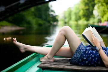 Legs of woman lying and reading a book on a boat by the water on a summer day