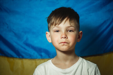 portrait of a serious little boy against the background of the flag of Ukraine