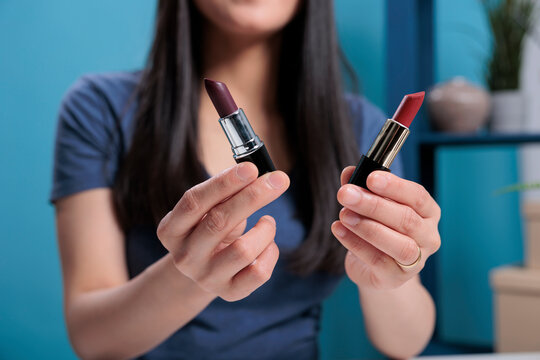 Asian content creator holding two lipstick showing at camera recording makeup tutorial advertising cosmetic product for vlogging channel. Social media influencer flming beauty review. Close up