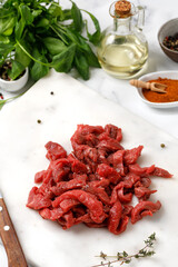 Cut raw beef, chopped meat, Beef strips for goulash on white cutting board with salt, dried herbs, oil.