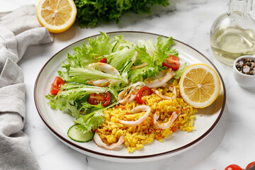 Seafood dish with squid rings, rice, green vegetable salad with tomatoes, cucumber on white plate.