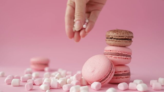 Close up of woman hands in pink shirt decorating macaroons and marshmallow on a pink background