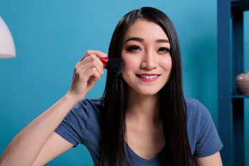 Portrait of asian influencer doing makeup tutorial in front of camera while recording content creator for vlogging channel. Vlogger woman using cosmetics brush advertising make up product - obrazy, fototapety, plakaty