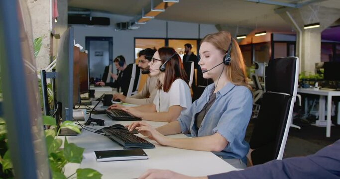 Caucasian beautiful cheerful woman in headset working at computer and talking with client in office. Support team. Worker of call center. Pretty female chatting with customers. Selling online by phone