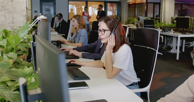 Caucasian woman working in call center and talking with client. Female worker in headset at support office. People speaking and helping to clients by phone line. Connection concept. Work online.