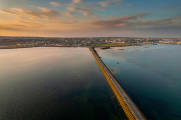 Causeway to Mutton island and Galway bay, town center in the background, Cloudy sky. Ireland. Blue ocean water at sunset. Irish landscape. Aerial view