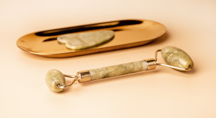 Gua Sha massage tools. Scraper and roller on golden stand and on beige background. Instruments for acupuncture therapy, trigger point treatment. High quality photo