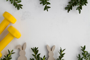 Two heavy dumbbells, boxwood branches and decorative wooden Easter bunnies. Healthy fitness lifestyle composition, gym workout and training concept. Fit flat lay frame with copy space.