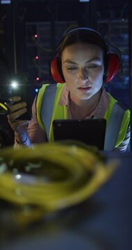 Vertical video of caucasian woman in high vis vest and ear guards using tablet in server room