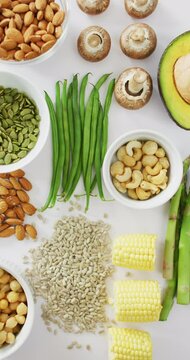 Vertical video of high angle of fresh avocado, beans, mushrooms, corn and asparagus on white