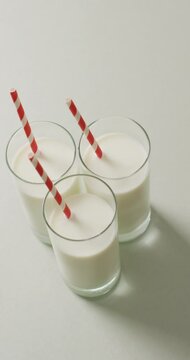Vertical video of three glasses of milk with red and white straw on grey background