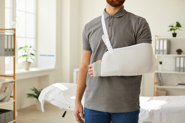 Unknown man wearing arm sling bandage on broken arm is standing in medical office. Cropped image of...