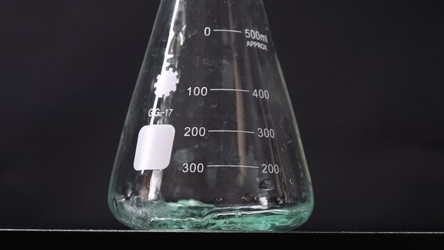Close-up of a green liquid being poured into a flask. Scientific background.