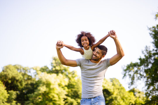 Portrait Of Happy Black Father Carrying Daughter On Back Outdoors. Family Happiness Love Concept.