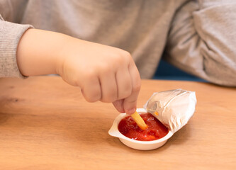 Child boy eating his French fries with ketchup in the cafe. Junk food, unhealthy eating concept