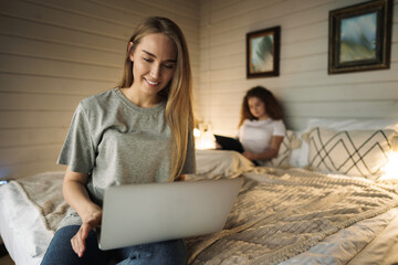 Two beautiful women lying in bed, holding a laptop