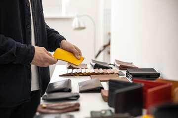 Craftsman hands laying out leatherwork on wooden showcase at leather workshop. Handwork accessories