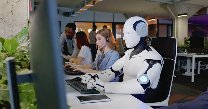 Robot working at computer among people. Android typing on keyboard in office. IT team of future. Futuristic worker. Humanoid work at call center. Support job. Selling concept. Technologies.