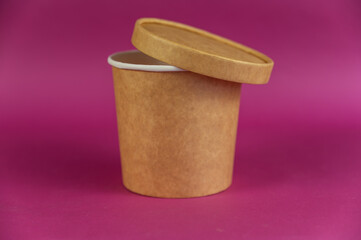 Empty cylindrical paper container with lid opposite-colored background. Brown food container for soup, ice cream, noodles, or other food.