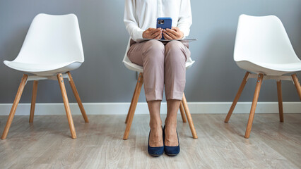 Studio shot of an attractive young businesswoman sitting down on a chair and using her cellphone. Businesswoman using a smartphone while in line waiting against a gray background