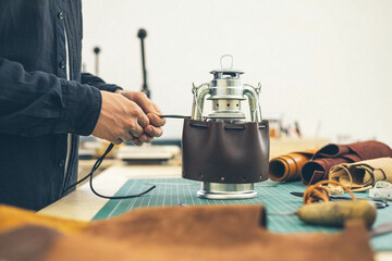Male tanner working makes a leather case for a camping kerosene lamp.