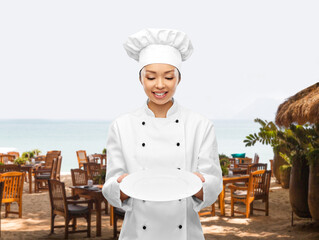 cooking, culinary and people concept - happy smiling female chef holding empty plate over open-air...