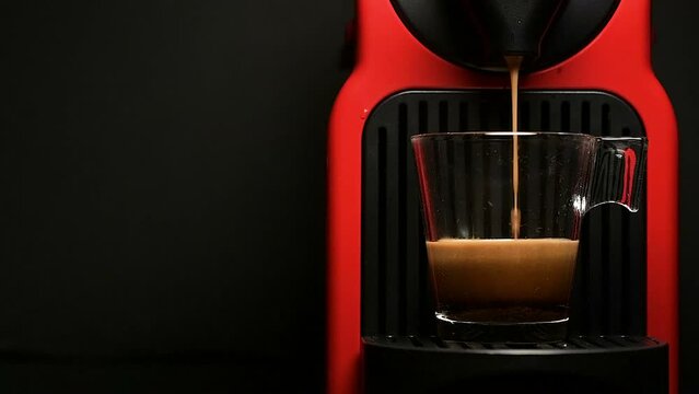 Process of making coffee by coffee machine into glass transparent cup - espresso coffee coming out from home coffemaker machine - On black background - In slow motion.