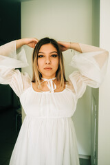Naklejka premium Portrait of attractive caucasian young woman in a white dress standing in a empty room with white walls.