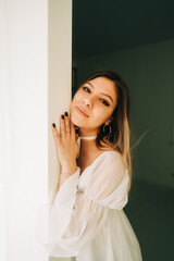 Portrait of attractive caucasian young woman in a white dress standing in a empty room with white walls.