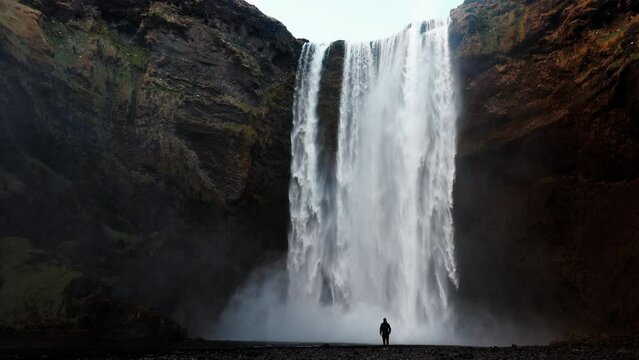 Man standing near the Icelandic waterfall Skogafoss in Iceland, near the Skogar, slow-motion background wallpapers. Beautiful landscape. High quality 4k footage. Wide angle shot