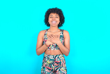 Happy smiling young woman with afro hairstyle in sportswear against blue background has hands on...