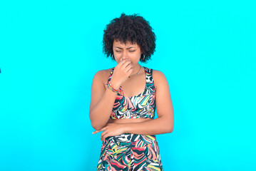 young woman with afro hairstyle in sportswear against blue background , holding his nose because of a bad smell. - obrazy, fototapety, plakaty