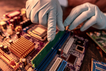 The engineer's gloved hand holds the computer's RAM chip against the background of the motherboard