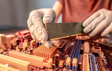 A repair engineer holds a RAM chip with his hands, inserts the RAM into the socket of the computer's motherboard