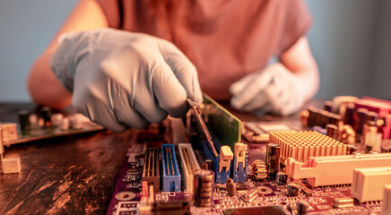 A repair engineer holds a RAM chip with his hands, inserts the RAM into the socket of the...