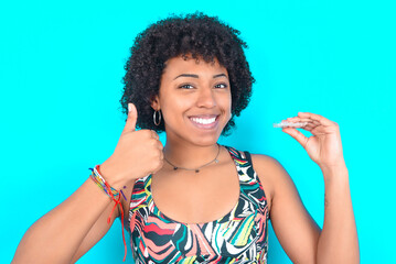 young woman with afro hairstyle in sportswear against blue background holding an invisible braces...