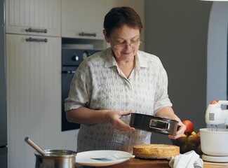 An elderly woman in the kitchen makes a cake. Healthy homemade food.