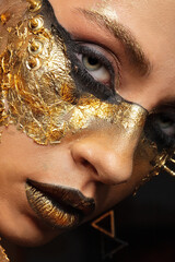 Closeup portrait of beautiful young woman with golden foil on face. Creative golden makeup on black background
