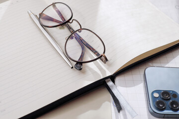 Office. On the table is a pen, diary, mobile phone, glasses.