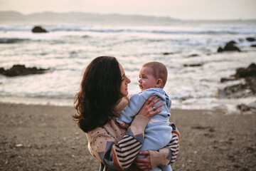 Single young mother holding and looking at her baby on the beach