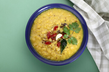 Indian food tuvar Daal or yellow lentil soup or curry in blue ceramic bowl on green background
