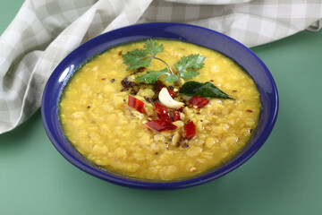 Indian food tuvar Daal or yellow lentil soup or curry in blue ceramic bowl on green background