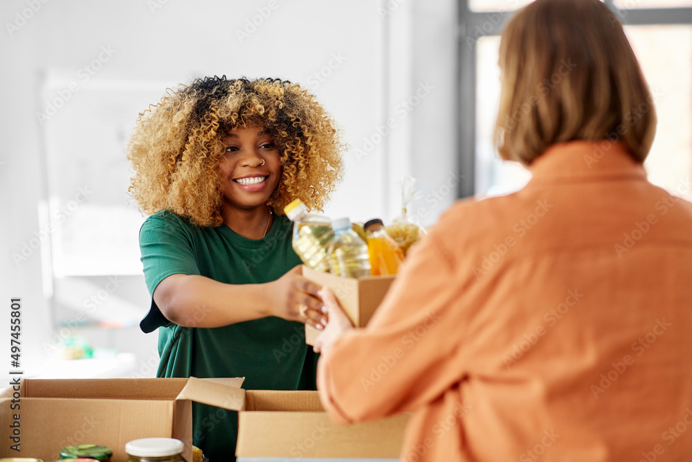 Wall mural charity, donation and volunteering concept - happy smiling female volunteer and woman taking box of 