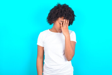 Fototapeta na wymiar young woman with afro hairstyle wearing white T-shirt against blue wall with sad expression covering face with hands while crying. Depression concept.