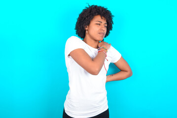 Fototapeta na wymiar young woman with afro hairstyle wearing white T-shirt against blue wall got back pain