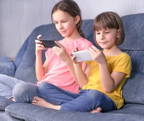 Fotobehang Lieve mosters Twee meisjes surfen op internet. Jonge meisjes die telefoon gebruiken, plezier hebben, naar het scherm kijken, video kijken of online chatten in een sociaal netwerk.